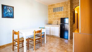 A kitchen with a stone wall, white cabinets, a black refrigerator, and a dining table with chairs. - Apartment 'Residence Eriguez - 8' with Shared Pool, Wi-Fi and Air Conditioning (Marina di Mancaversa)