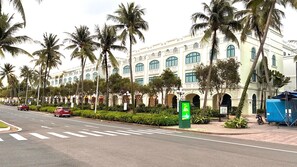 A street with a large building featuring arched windows and a symmetrical facade, surrounded by palm trees. -  Diamond Suite Lotus Village (Phu Quoc)