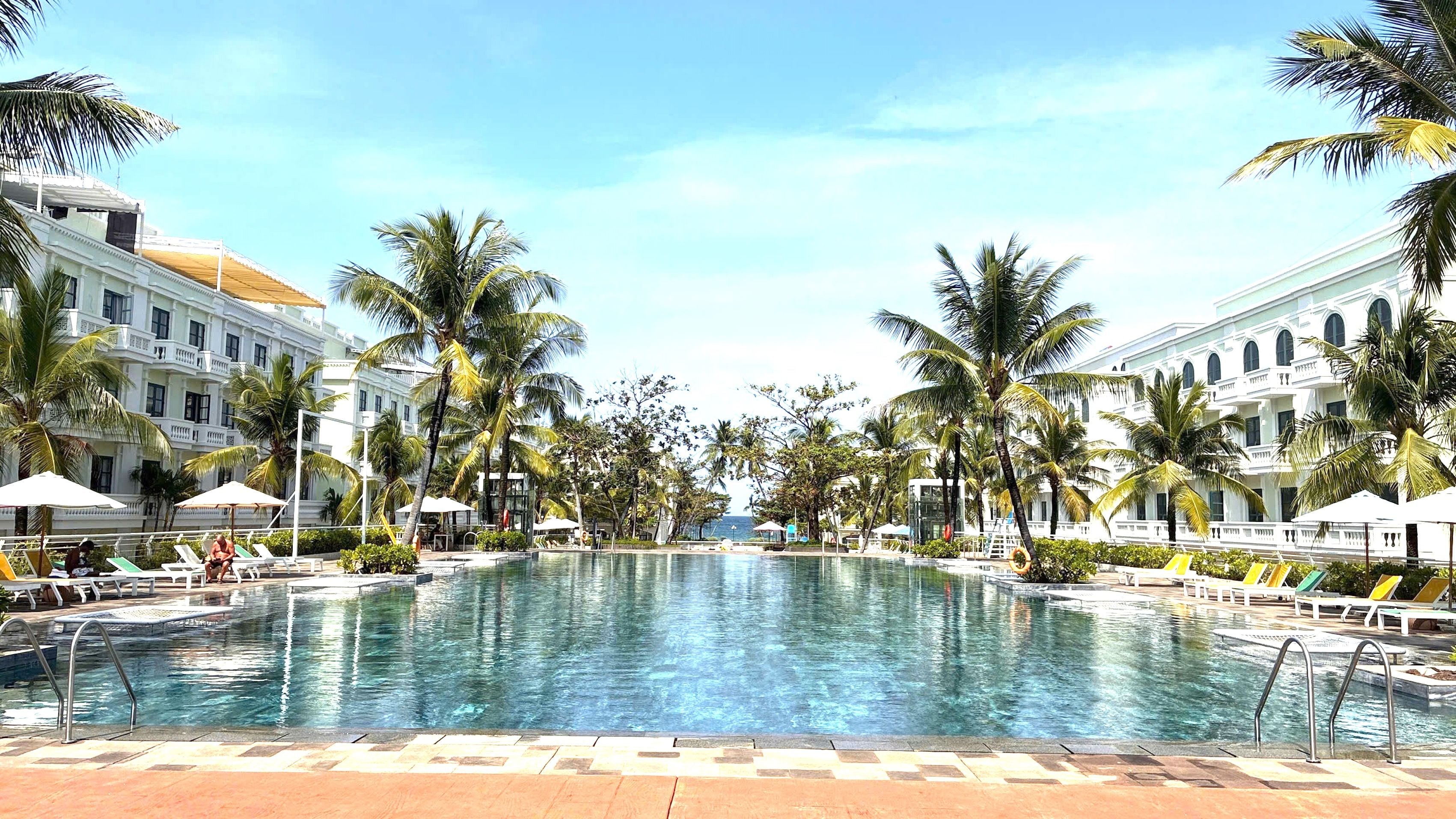 Una piscina rodeada de palmeras y edificios blancos con balcones.