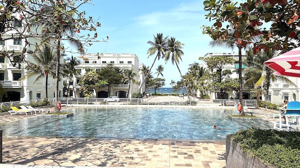 A swimming pool with lounge chairs and palm trees, surrounded by buildings. - Diamond Suite Lotus Village (Phu Quoc)