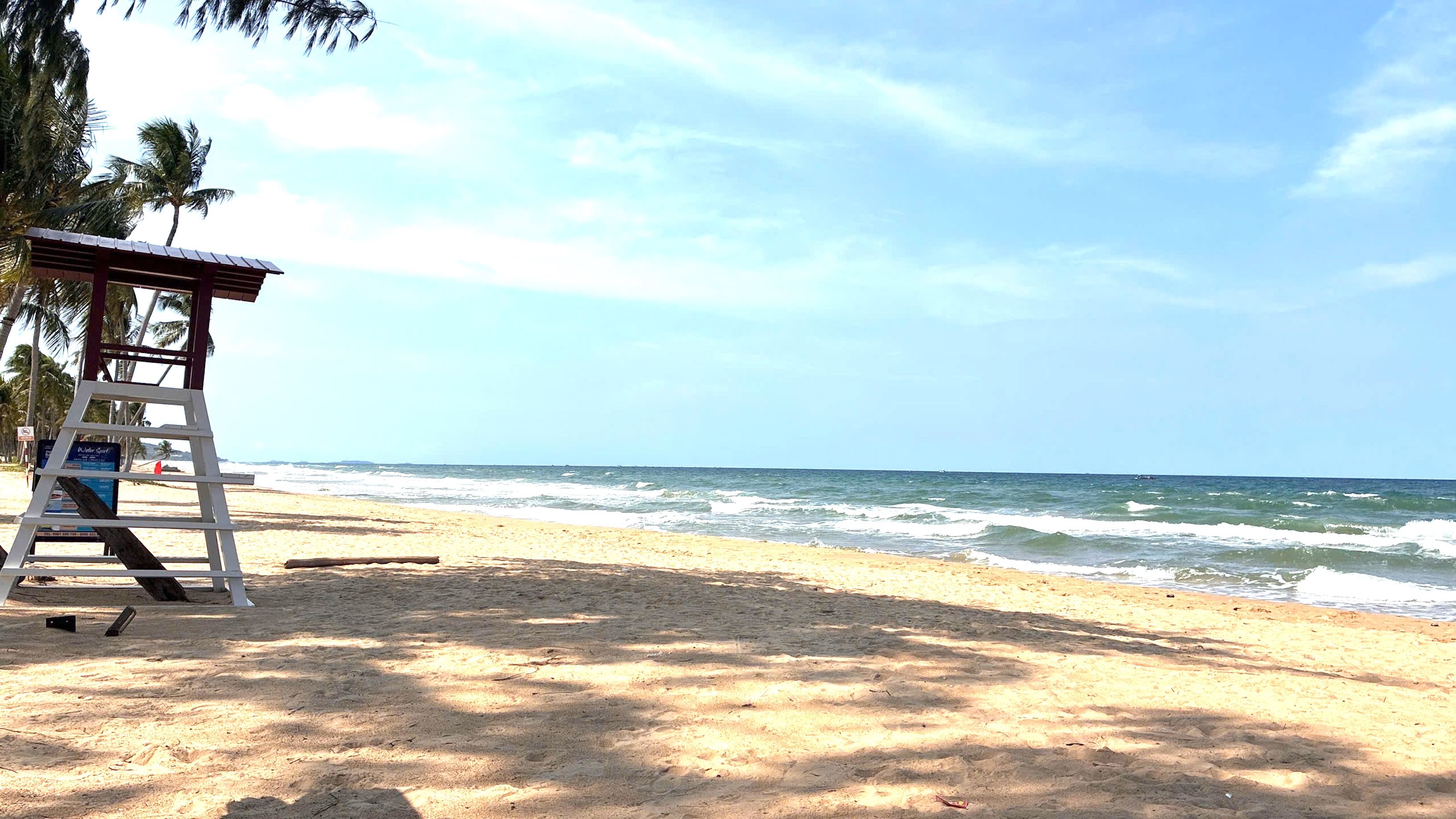Una playa con una torre de salvavidas, palmeras y olas del océano.