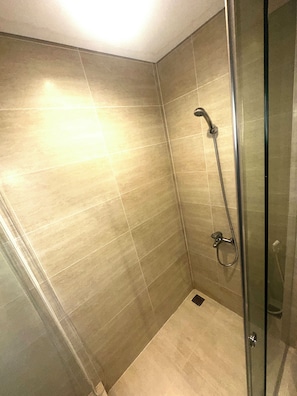 Ducha con mampara de vidrio, cabezal de ducha de mano y grifo empotrado.