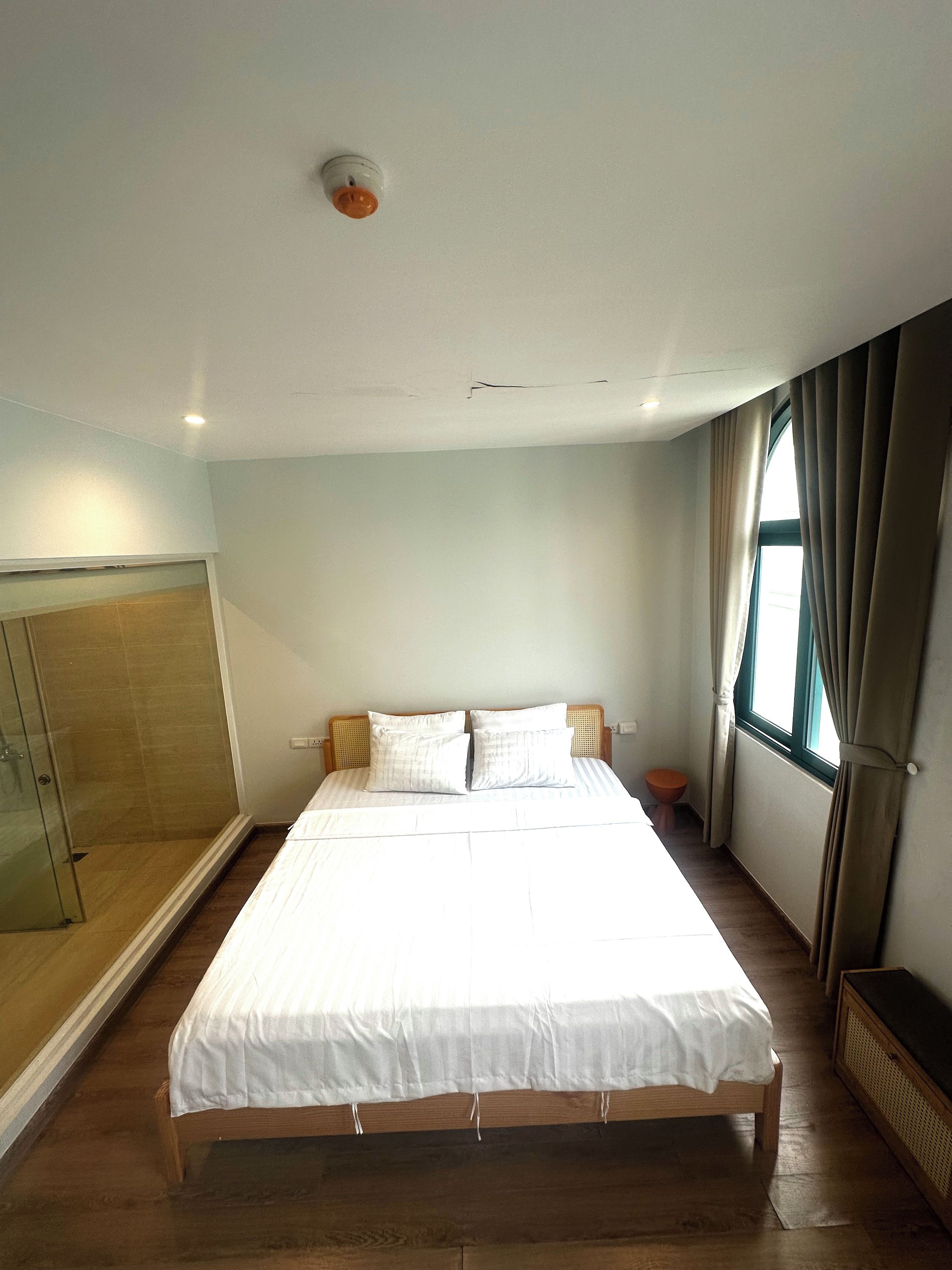Un dormitorio con una cama grande, un armario de madera, una cabina de ducha de vidrio y una ventana con cortinas.