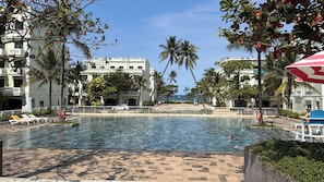 Una piscina con sillas de descanso y palmeras, rodeada de edificios con balcones.