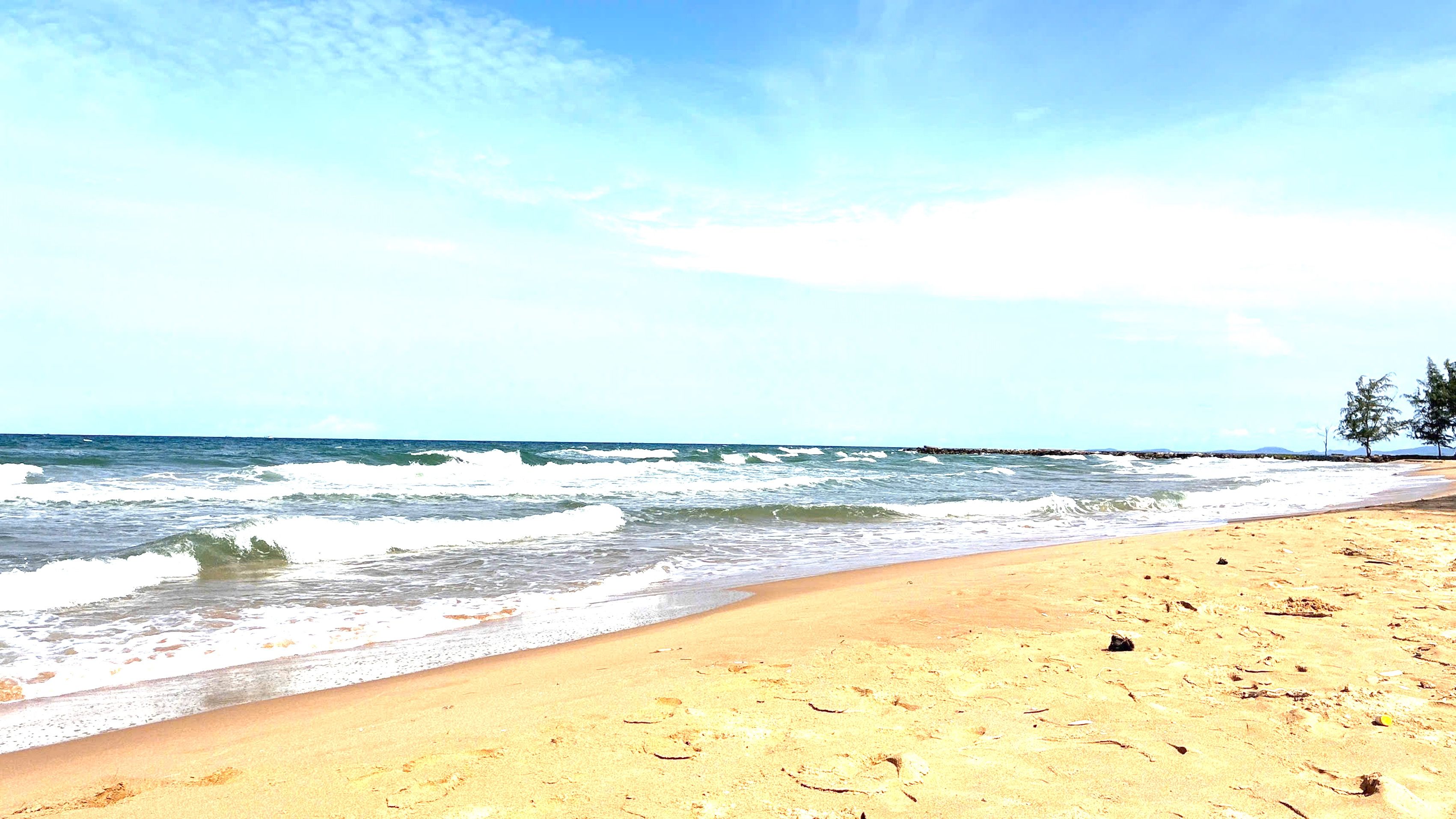 A beach with waves, a clear sky, and a distant shoreline.