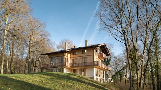 A two-story house with a balcony on the upper floor, surrounded by trees and a grassy hill. - bel Etage Avenue in the Parkchalet (Potsdam)