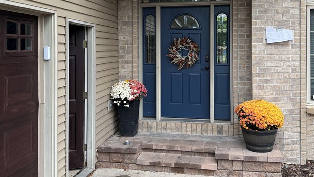 A two-story house with a blue front door, a brick exterior, and two flower pots on the front porch. - EAA Exquisite 6-bedroom 3.5 bathroom house w AC on water only 8 minutes from EAA (Oshkosh)