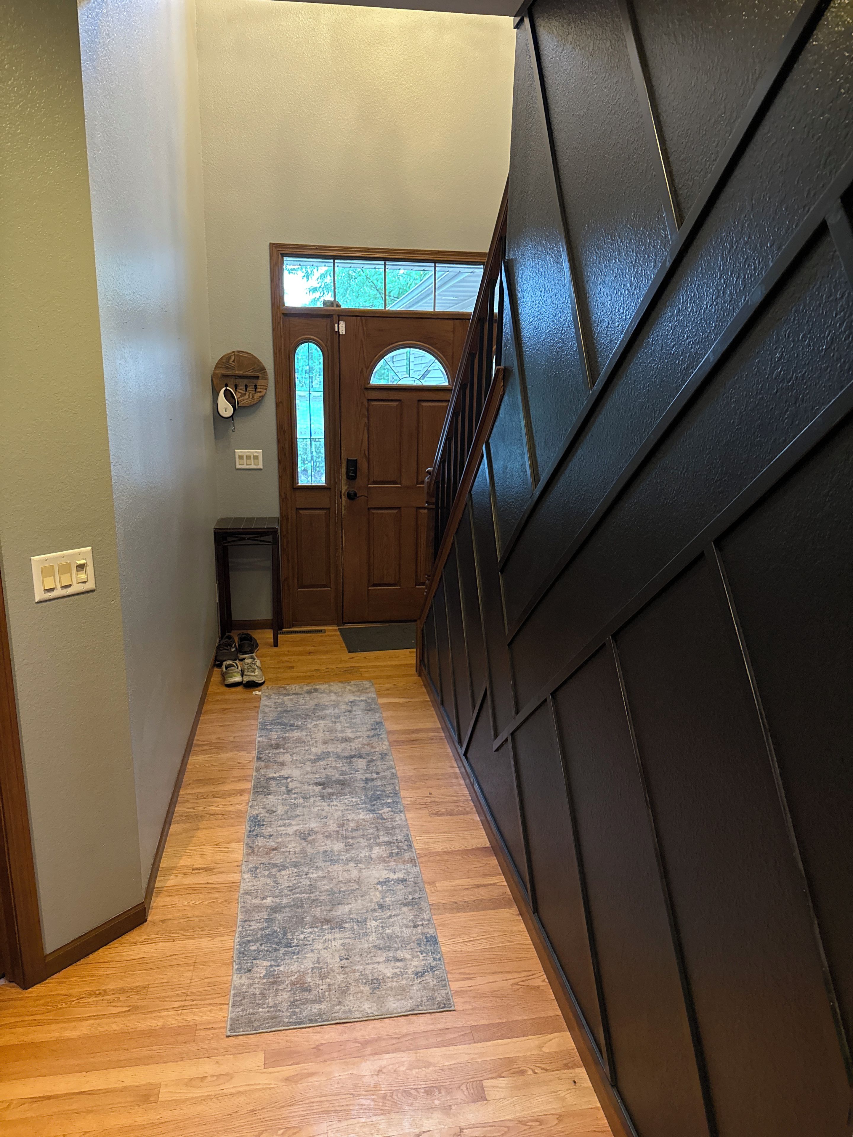 Un couloir avec une porte en bois, un tapis et un escalier.