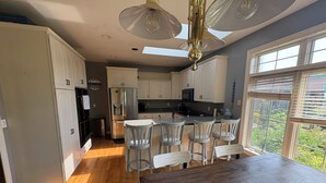 A kitchen with white cabinets, a stainless steel refrigerator, a built-in oven, a microwave, and a sink. There is a wooden dining table with four chairs. - EAA Exquisite 6-bedroom 3.5 bathroom house w AC on water only 8 minutes from EAA (Oshkosh)
