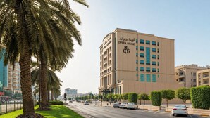 A multi-story building with a sign reading 'OPERA GRAND' and a palm tree-lined street. - Opera Grand Hotel Deira (Dubai)