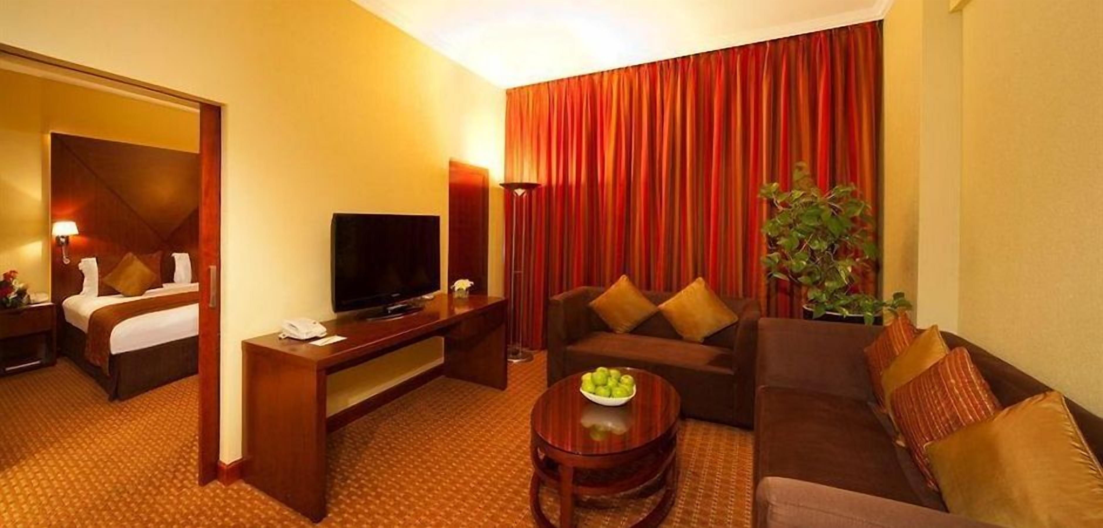Una camera d'albergo con un letto, una televisione, un divano, un tavolino da caffè e una pianta.