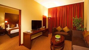 A hotel room with a bed, a TV, a sofa, a coffee table, and a plant. - Opera Grand Hotel Deira (Dubai)