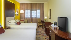 A hotel room with two beds, a television, a desk with a lamp, and a window with curtains. - Opera Grand Hotel Deira (Dubai)