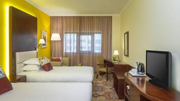 Quarto de hotel com duas camas, televisão, escrivaninha com luminária e janela com cortinas.