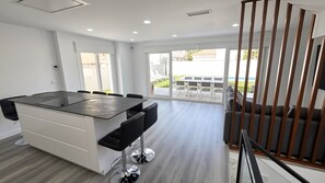 Een moderne keuken met een centraal eiland, een eethoek met stoelen en uitzicht op een binnenplaats door grote ramen.