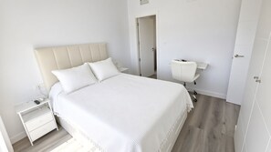 A bedroom with a bed, nightstand, chair, and a door.