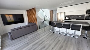 Een moderne keuken met een inbouwkoelkast, een eethoek met barstoelen en een grijze bank.