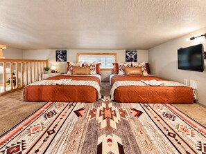 A bedroom with two beds, a large rug, and a TV on the wall. - Lake Travis Cabin Retreat + Pool, Hot Tub, Gym (Austin)