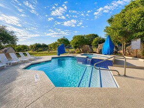 A swimming pool with a blue water feature, surrounded by lounge chairs and covered umbrellas. - Lake Travis Cabin Retreat + Pool, Hot Tub, Gym (Austin)