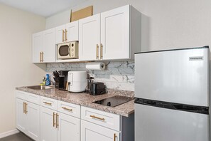 Eine moderne Küche mit weißen Schränken, einem Edelstahlkühlschrank, einer Mikrowelle, einer Kaffeemaschine und einem Toaster.