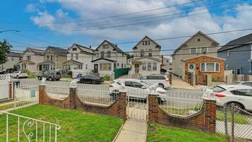 Una calle residencial con casas, automóviles y un acceso enrejado con estatuas decorativas.
