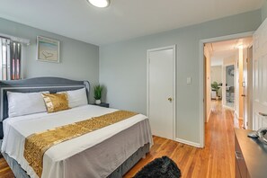 A bedroom with a bed, bedside tables, a door, and a hallway leading to a bathroom. - 3 Mi to Jfk: Convenient NYC Base w/ Shared Patio (Jamaica)