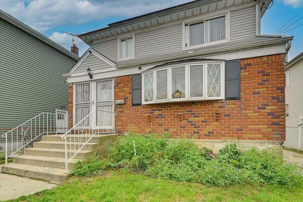 A two-story house with a brick facade, a front porch with steps, and a metal railing. - 3 Mi to Jfk: Convenient NYC Base w/ Shared Patio (Jamaica)