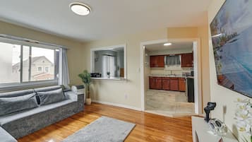 Una sala de estar con un sofá gris, piso de madera y vista al exterior.