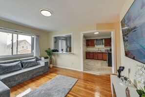 A living room with a grey sofa, a wooden floor, and a view of the outside. - 3 Mi to Jfk: Convenient NYC Base w/ Shared Patio (Jamaica)