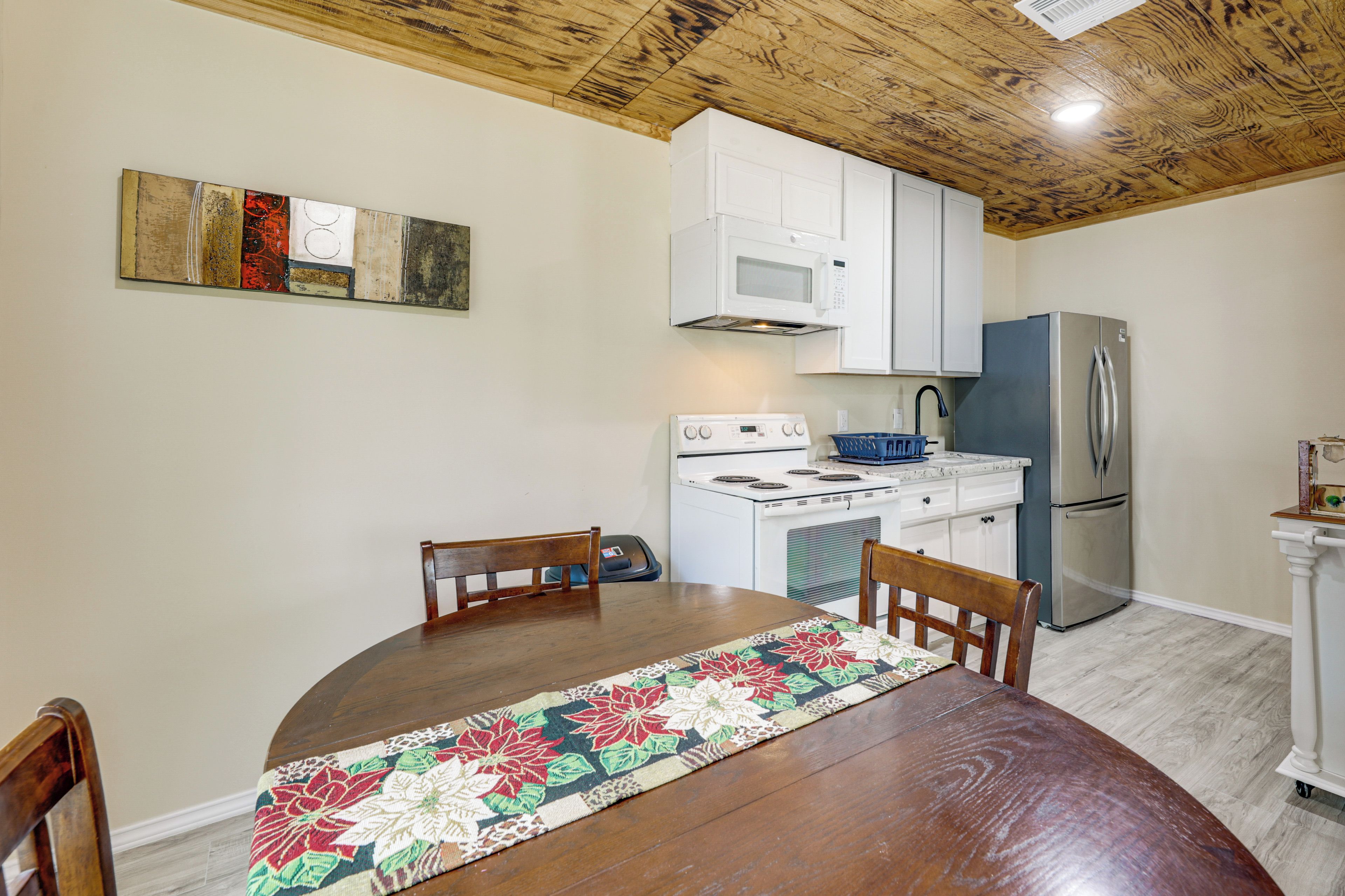 A dining area with a wooden table, chairs, a kitchen with white cabinets, a stove, and a refrigerator.