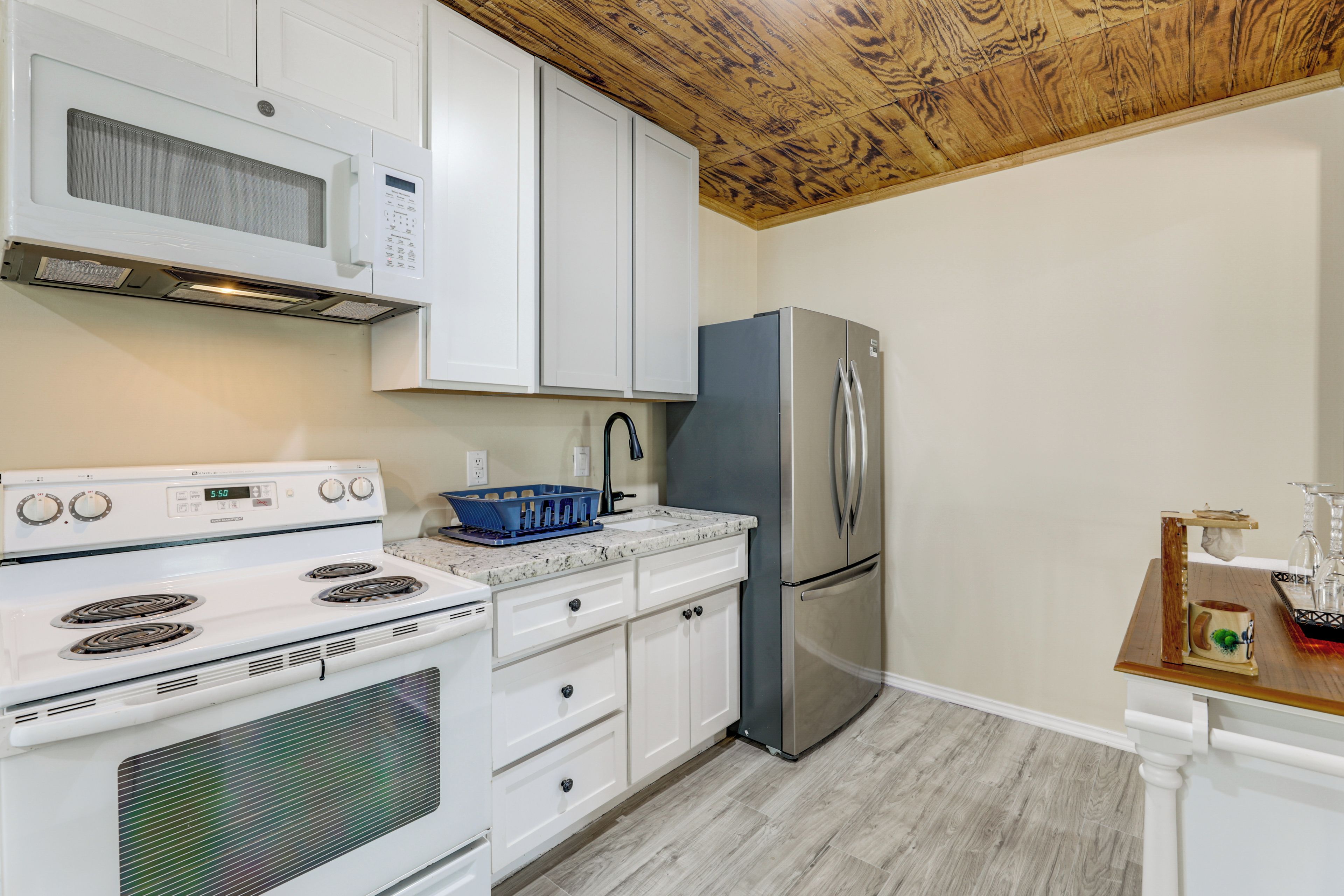 A kitchen with white cabinets, a stainless steel refrigerator, a white stove, and a wooden ceiling.