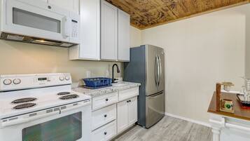 A kitchen with white cabinets, a stainless steel refrigerator, a white stove, and a wooden ceiling.