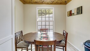 Uma sala de jantar com mesa de madeira, quatro cadeiras, janela com persianas e um quadro na parede.