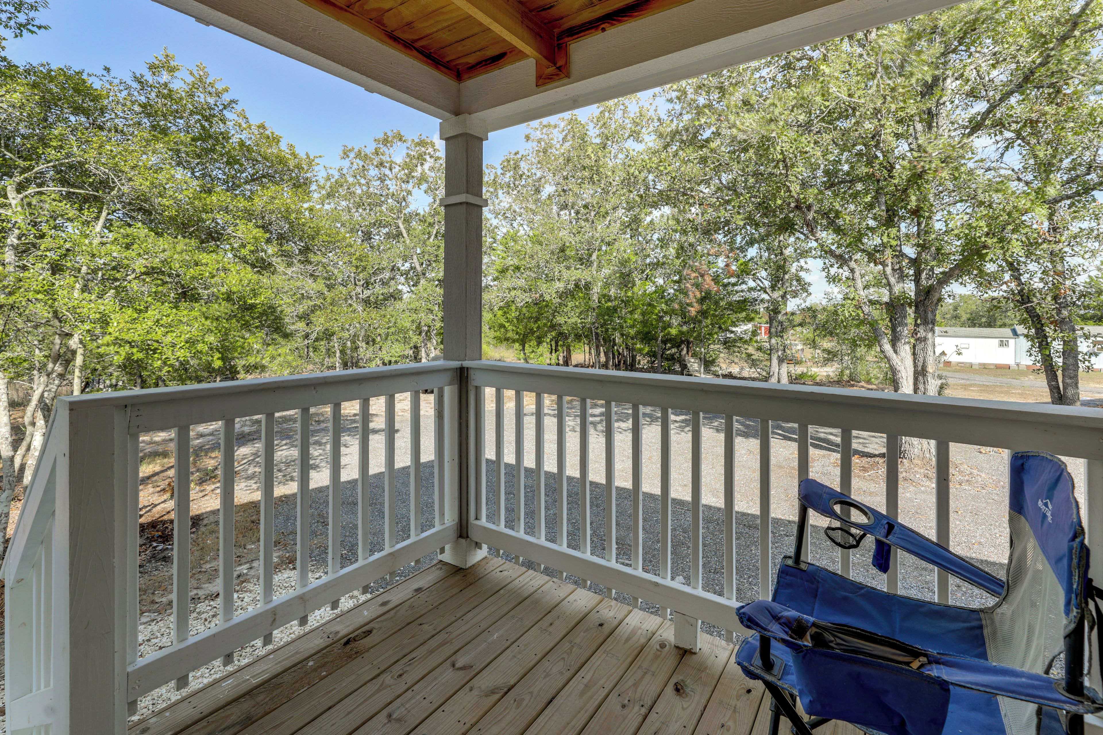 A wooden deck with a white railing, a blue folding chair, and trees in the background.