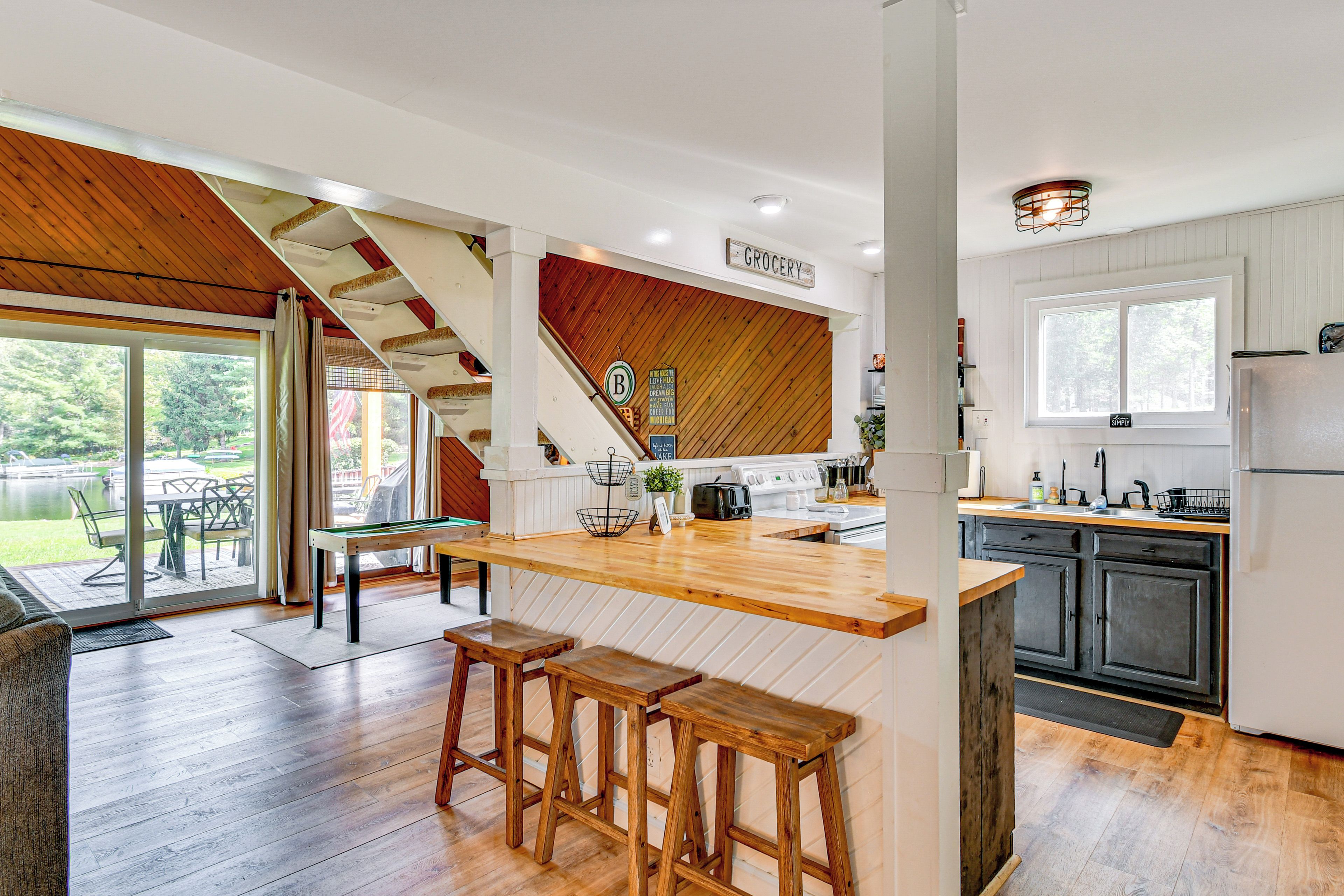 A modern kitchen with wooden accents, a dining area with stools, and a view of the outdoors.