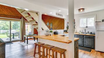 A modern kitchen with wooden accents, a dining area with stools, and a view of the outdoors.