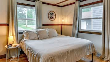 A bedroom with a bed, a bedside table with a lamp, a wall clock, and a window with curtains.