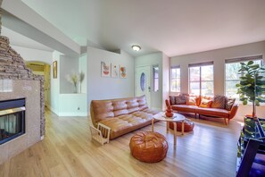 A spacious living room with a fireplace, a leather sofa, a coffee table, and a large window providing natural light.