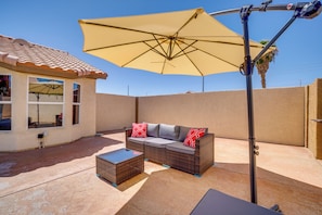A patio with a wicker sofa, a small table, and a large umbrella.