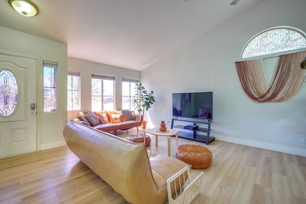 A living room with a sofa, ottoman, TV, and a decorative wall piece.