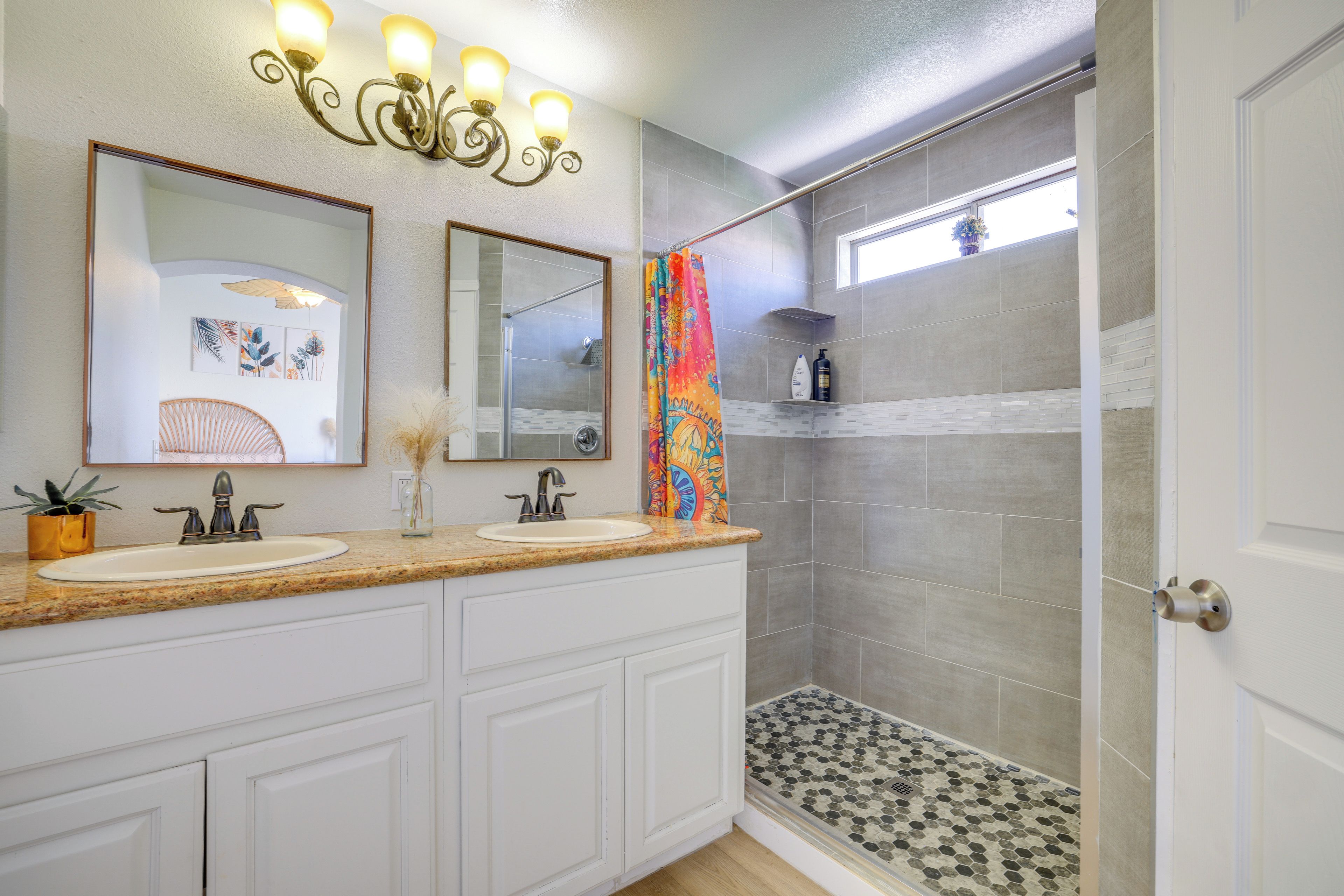 A bathroom with a double sink vanity, a shower with a glass door, and a decorative light fixture above the mirrors.