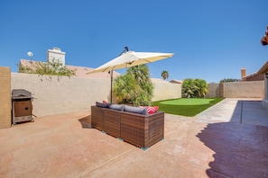 A patio with a wicker sofa, an umbrella, and a small lawn with a flag.