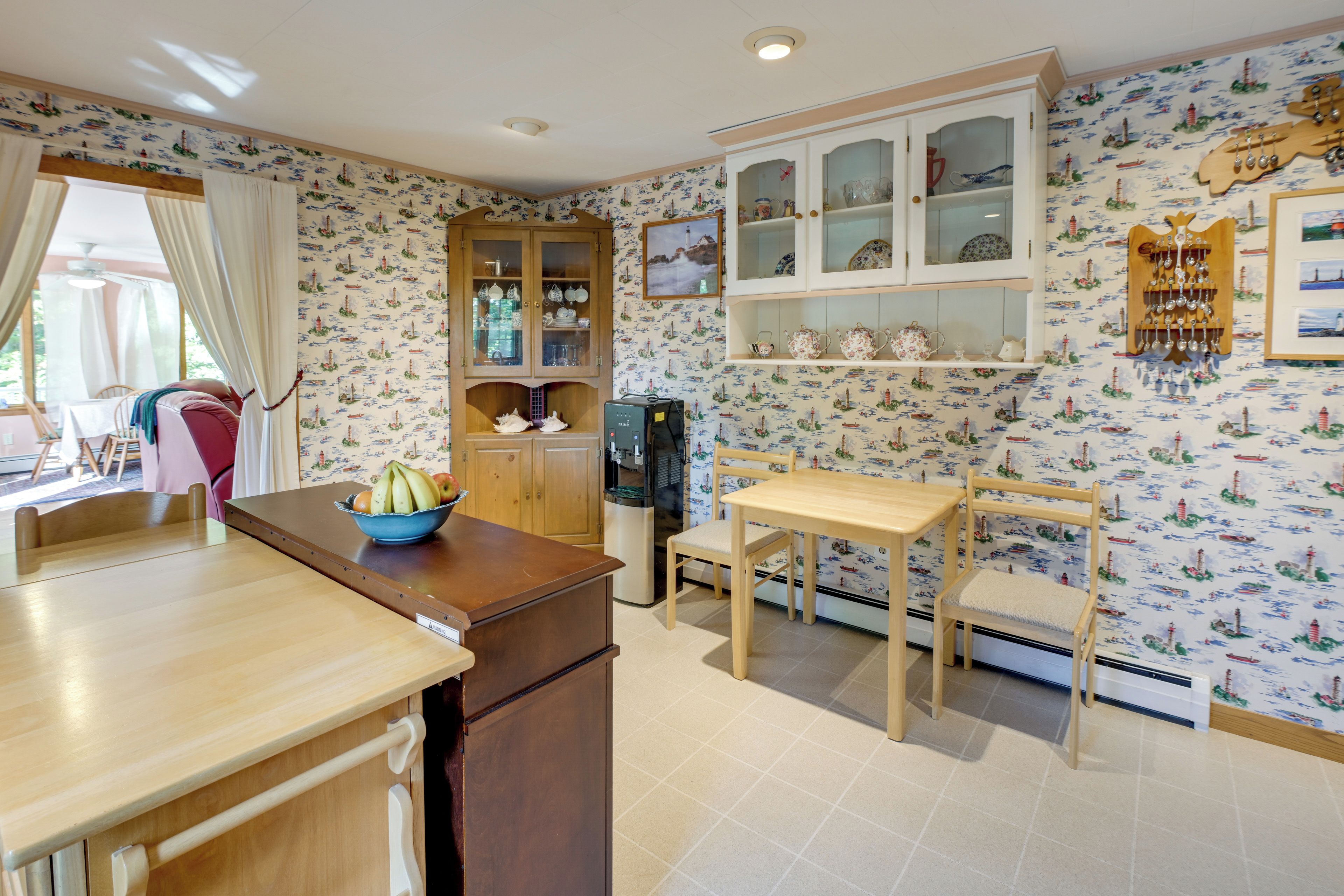 A kitchen with a wooden counter, a dining table with chairs, a fruit bowl, and a cabinet with glass doors.