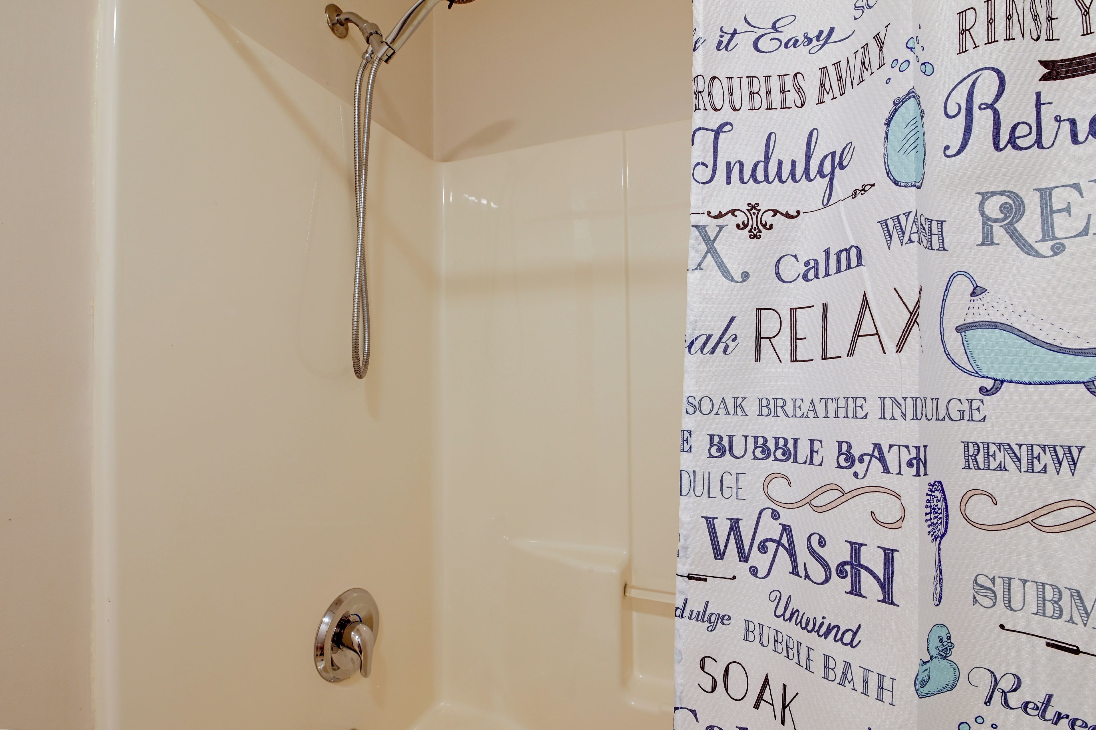 A bathroom with a shower curtain featuring motivational phrases and a bathtub with a shower head.