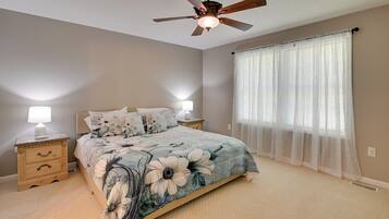 A bedroom with a bed, two bedside tables, a ceiling fan, and sheer curtains.