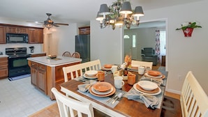A modern kitchen with a central island, wooden cabinets, and a dining area set for a meal. - Private Yard: Fire Pit & Cornhole! Moorefield Gem (Moorefield)