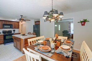 A modern kitchen with a central island, wooden cabinets, and a dining area set for a meal. - Private Yard: Fire Pit & Cornhole! Moorefield Gem (Moorefield)