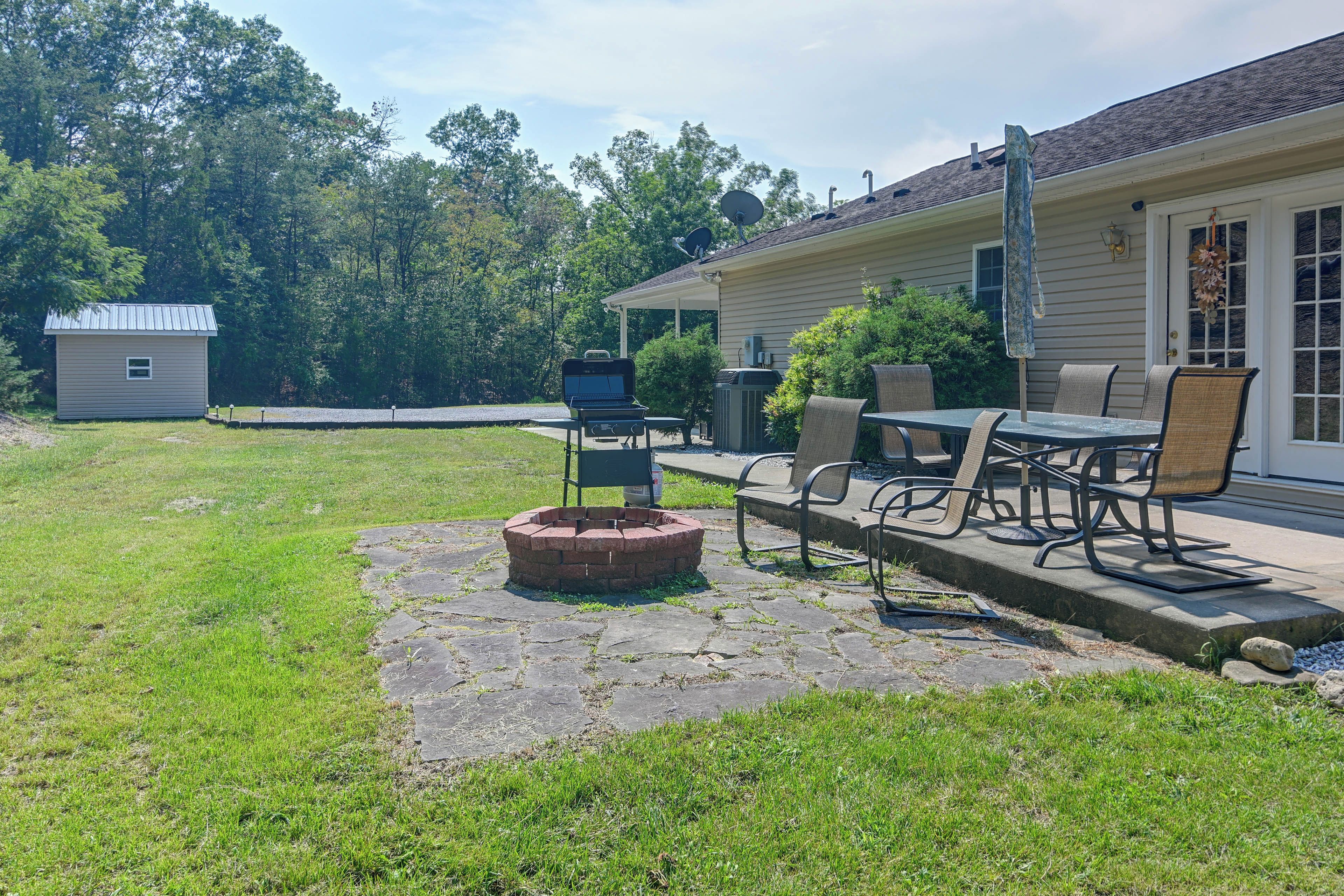 A backyard with a fire pit, outdoor furniture, and a house with a satellite dish.