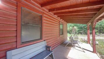 A wooden cabin with a porch, a bench, and a swing set.
