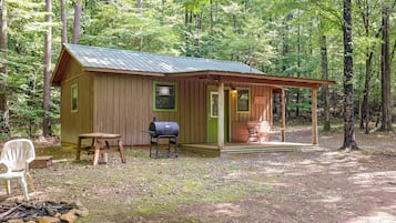 A rustic cabin with a porch, a grill, and a chair.